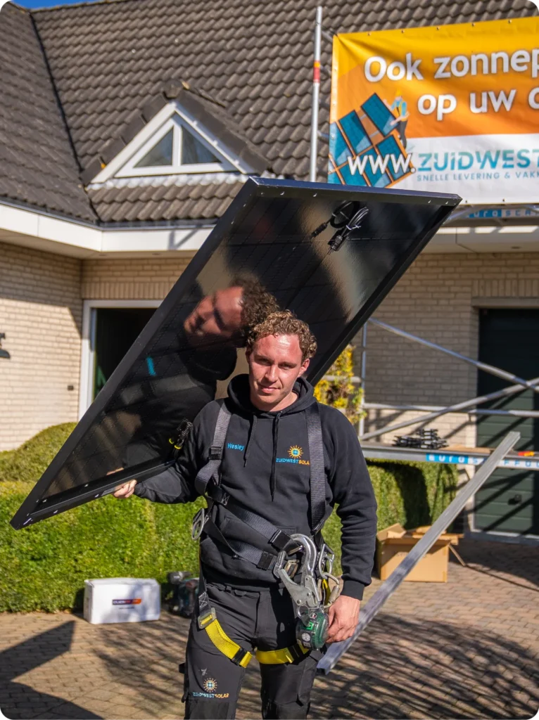 Monteur draagt een zonnepaneel voor een woning, met het ZuidWest Solar-spandoek op de achtergrond